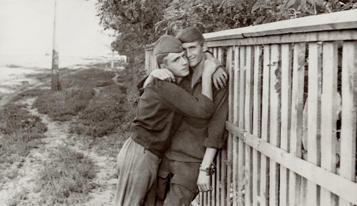 Vintage photograph of two young men embracing beside a wooden fence